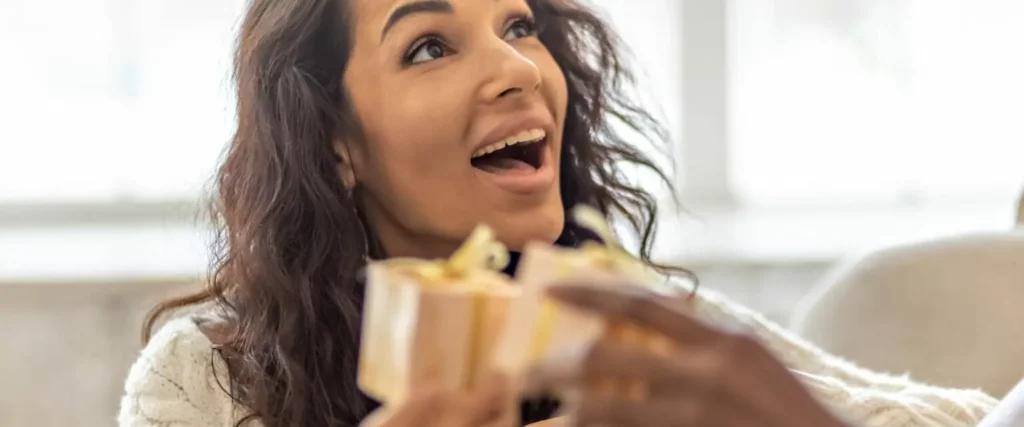 Mensch mit überraschtem Blick beim Auspacken von Goodiebag-Geschenken.